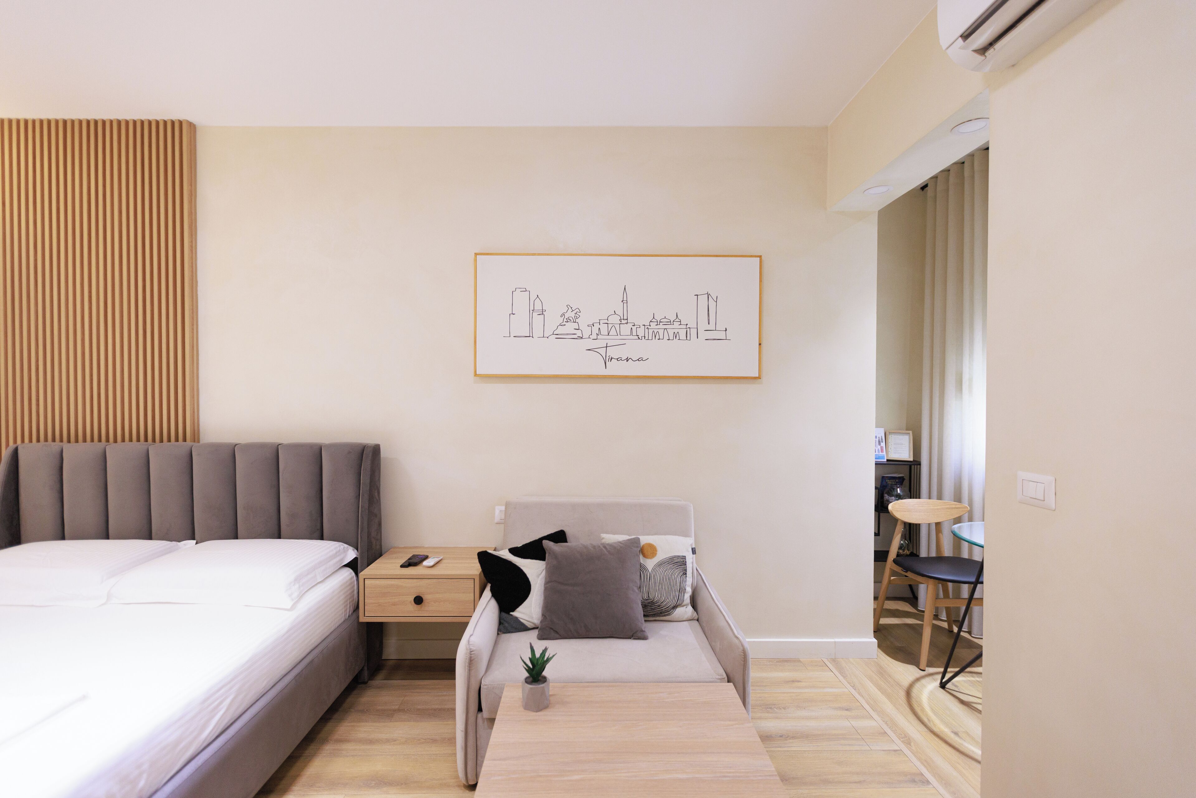 A modern bedroom with a bed, bedside table, and a small sofa. There is a framed cityscape artwork on the wall.