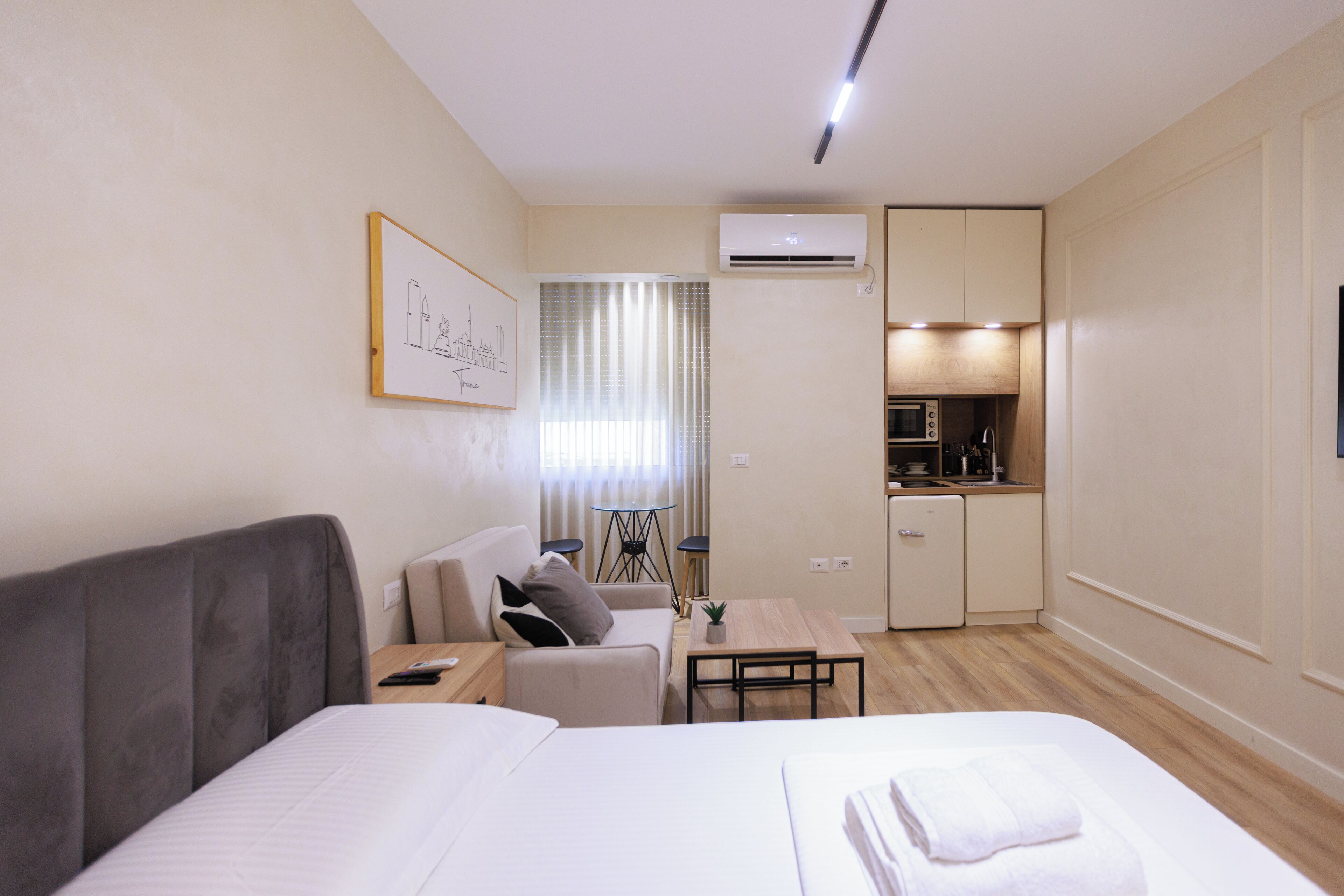 Una camera d'albergo con un letto, un divano, un tavolino, un angolo cottura e una finestra con tende.