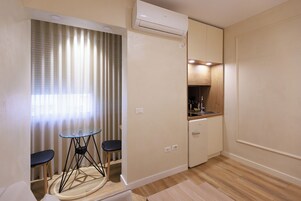 Habitación compacta con kitchenette, un pequeño comedor con una mesa y dos sillas, y una ventana con cortinas.