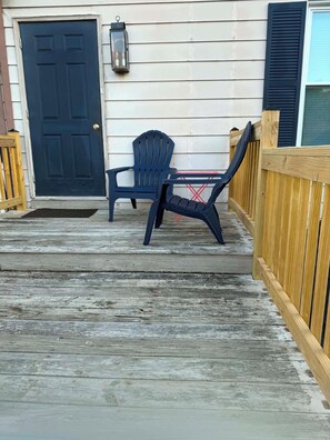 Een houten terras met een zwarte deur, een zwarte Adirondack-stoel en een kleine tafel.