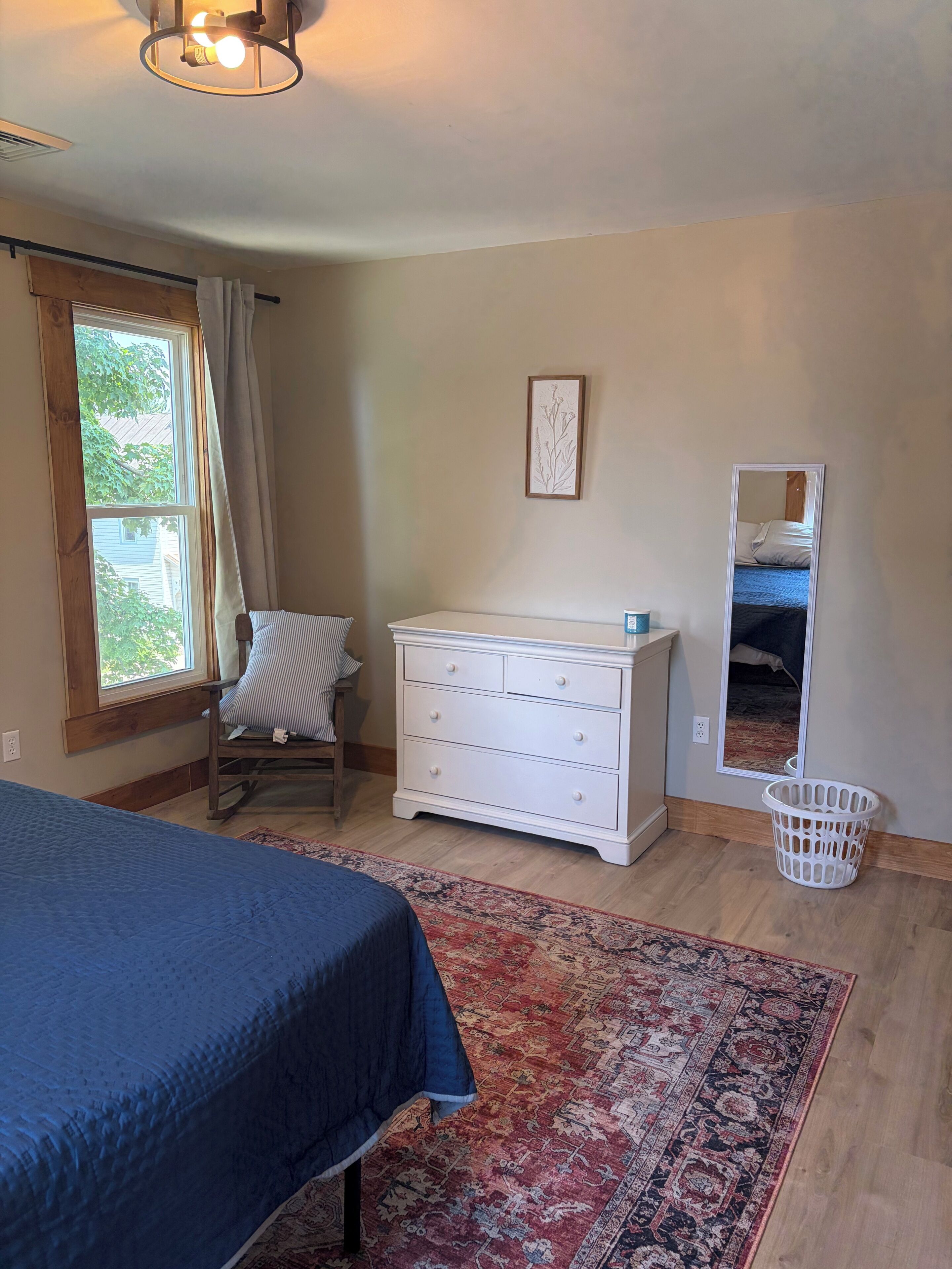 Ein Schlafzimmer mit Bett, Kommode, Stuhl, Fenster und Teppich.