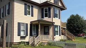 A two-story house with a front porch, a staircase leading to a deck, and a fenced yard.