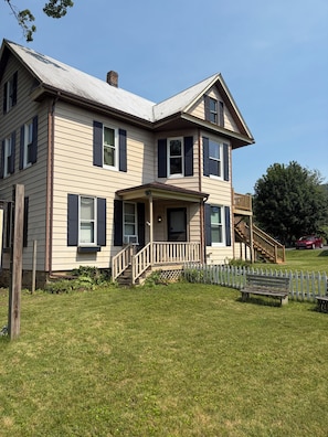 A two-story house with a front porch, a staircase leading to a deck, and a fenced yard.
