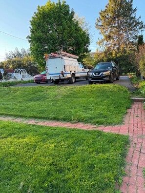 Un'area verdeggiante con un vialetto lastricato, un furgone di servizio e un'auto parcheggiata.