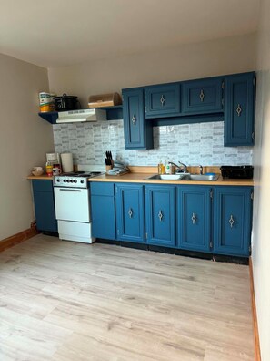 Een keuken met blauwe kastjes, een witte kookplaat en een betegelde achterwand.