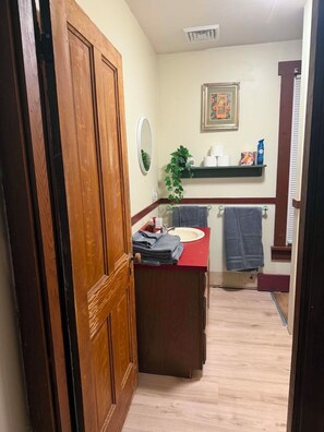 Een badkamer met een houten deur, een rode wastafel, een spiegel, een handdoekhouder en een plank met toiletartikelen.