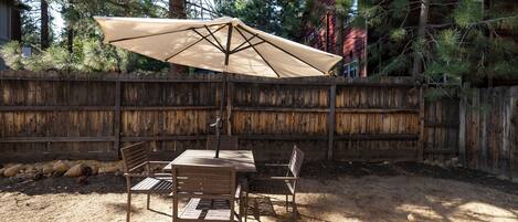 An outdoor patio with a table and chairs, a large umbrella, and a wooden fence.