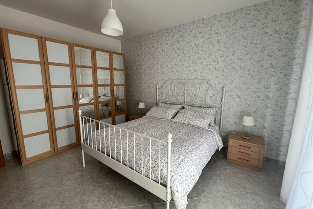 Un dormitorio con cama, mesitas de noche, armario y lámpara colgante.