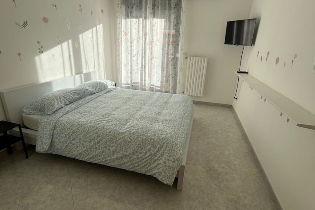 A bedroom with a bed, a chair, a TV, and a radiator.