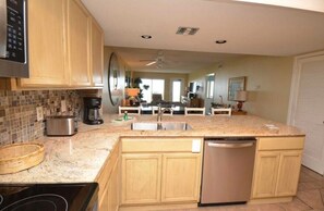A kitchen with wooden cabinets, a stainless steel dishwasher, a granite countertop, and a tiled backsplash. - Two Bedroom Two Bath Beachfront Condo (South Padre Island)