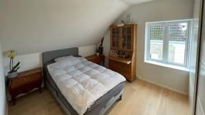 A bedroom with a bed, wooden nightstands, a dresser, a window, and a sloped ceiling.