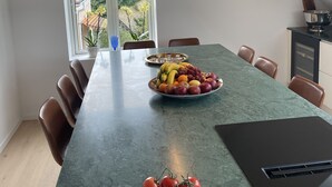 A dining area with a long table, chairs, a fruit bowl, and a bowl of vegetables.