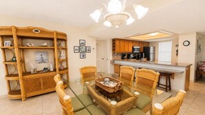 A dining area with a glass-top table surrounded by wicker chairs and a rattan console table with decorative items. - Three Bedroom Two Bath Beachfront Condo (South Padre Island)