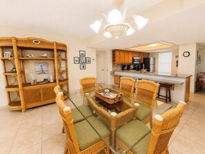 A dining area with a glass-top table surrounded by wicker chairs and a rattan console table with decorative items. - Three Bedroom Two Bath Beachfront Condo (South Padre Island)