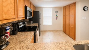 A kitchen with wooden cabinets, a microwave, a refrigerator, and a granite countertop. - Three Bedroom Two Bath Beachfront Condo (South Padre Island)