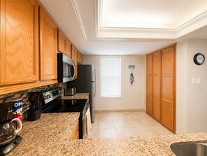 A kitchen with wooden cabinets, a microwave, a refrigerator, and a granite countertop. - Three Bedroom Two Bath Beachfront Condo (South Padre Island)