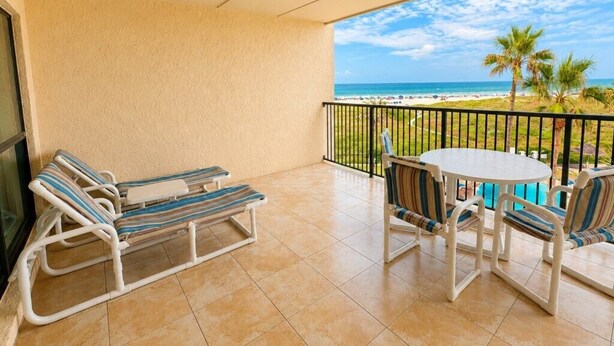 A balcony with a view of the beach, a table, and two lounge chairs. - Three Bedroom Two Bath Beachfront Condo (South Padre Island)