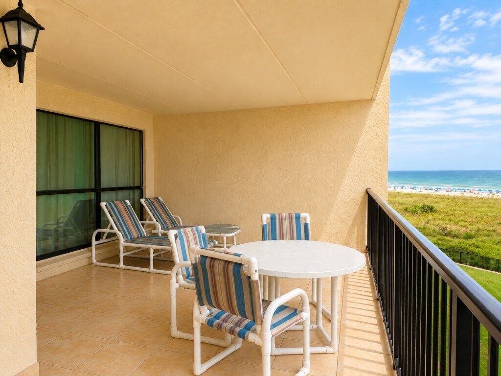 Un balcon avec une table ronde et des chaises à rayures, donnant sur une plage.