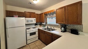 Una cocina con armarios de madera, un refrigerador blanco, un microondas, una estufa, un fregadero y una ventana con persianas.
