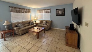 Una sala de estar con un sofá modular, una mesa de centro, una lámpara, un televisor y un aparador.