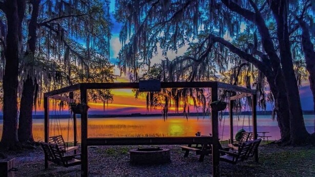 Un pabellón con vistas a un atardecer sobre el agua, rodeado de árboles.