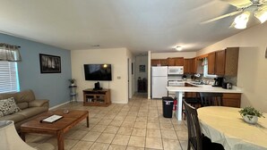 Una sala de estar con televisión, sofá, mesa de centro y un comedor con mesa y sillas.