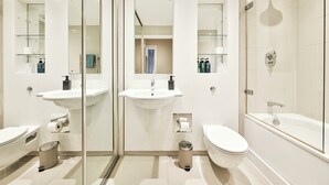A modern bathroom with two sinks, a toilet, a bathtub, and a shower. - Luxury One-Bedroom by Tower of London • Prime Location (London)