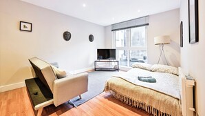 A modern bedroom with a bed, a sofa, a TV, and a window. - Luxury One-Bedroom by Tower of London • Prime Location (London)