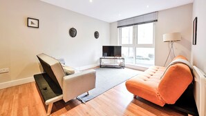 A modern living room with a sofa, a recliner, a flat-screen TV, and a lamp. - Luxury One-Bedroom by Tower of London • Prime Location (London)