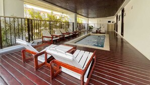 Ein überdachter Außenbereich mit Holzliegen, einem kleinen Pool und einem Bambuszaun.