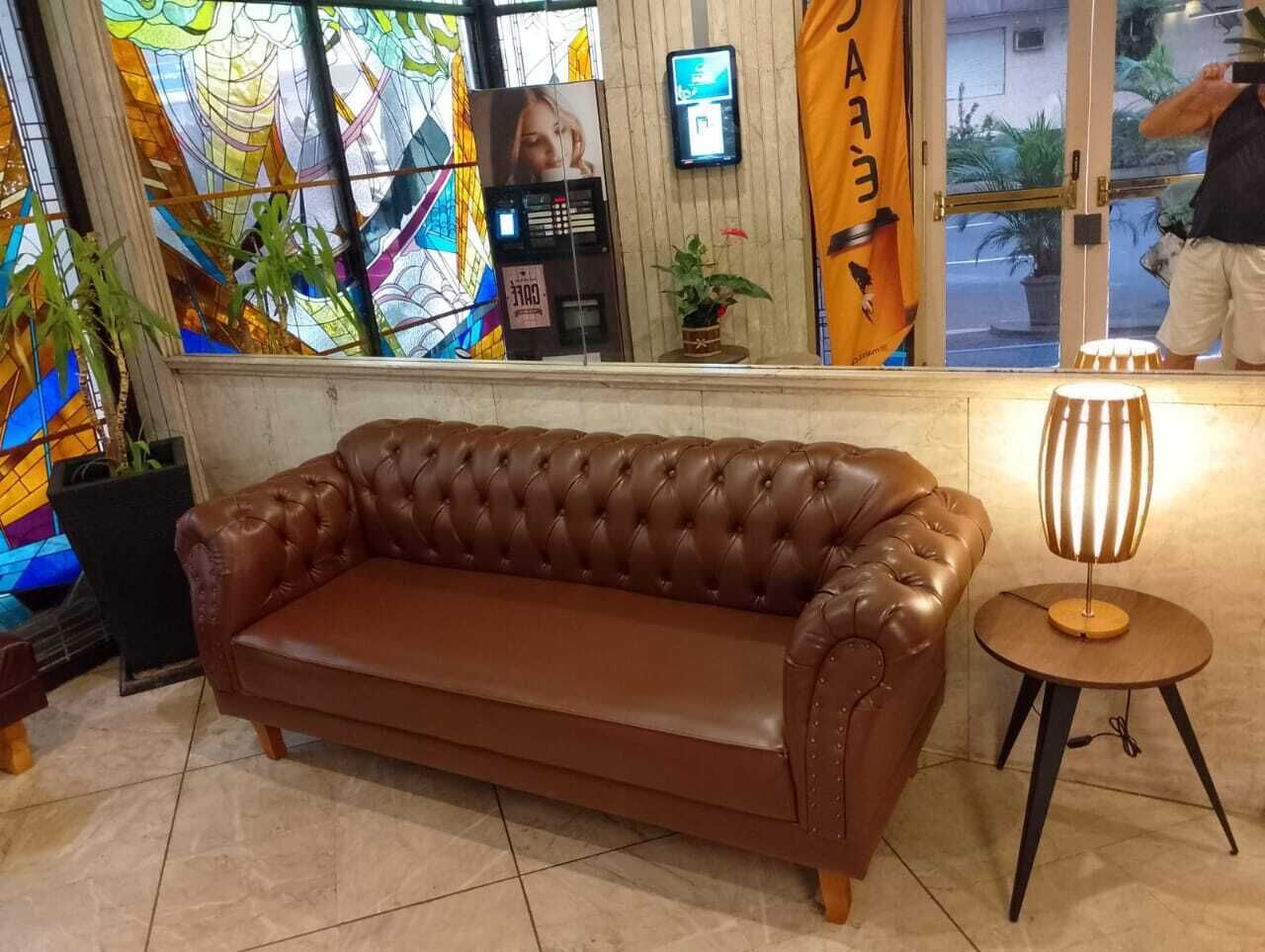 Un canapé en cuir marron dans un hall d’entrée, avec un vitrail, une petite table sur laquelle se trouve une lampe, et un panneau avec des caractères japonais.