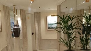 Eine geräumige Lobby mit Fliesenboden, einer großen Topfpflanze und einem gerahmten Bild an der Wand.