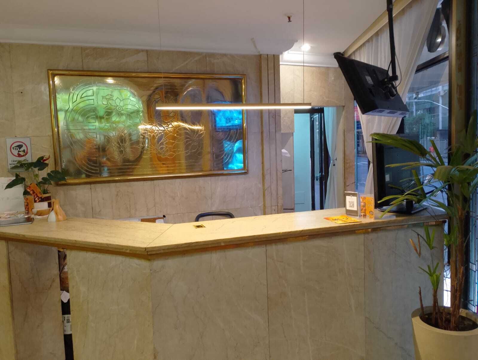 Een receptiebalie met daarboven een groot abstract schilderij, een televisie en een potplant.