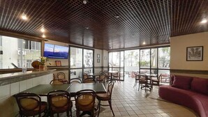 Ein Restaurant mit hoher Decke, Fliesenboden und großen Fenstern. Es sind Tische und Stühle für die Essenszeit bereitgestellt.