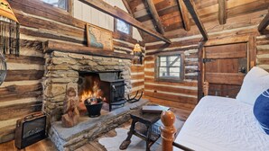 A log cabin interior with a stone fireplace, wooden beams, a bed, and a map on the wall. - Lodge at Wagon Gap Trl. 3 Blue Ridge River Cabins (Canton)