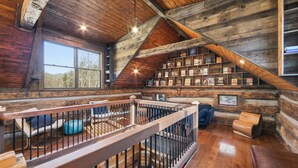 A log cabin interior with a wooden staircase, a bookshelf, and a view of the outdoors. - Lodge at Wagon Gap Trl. 3 Blue Ridge River Cabins (Canton)