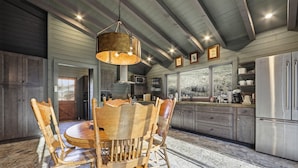 A rustic kitchen with wooden chairs, a large hanging light fixture, and a stone floor. - Lodge at Wagon Gap Trl. 3 Blue Ridge River Cabins (Canton)