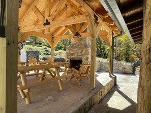 En paviljong av trä med en steneldstad, picknickbord och en skylt med texten ”CORKOUT COVE”.