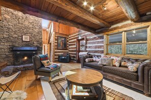 A cozy log cabin interior with a stone fireplace, leather furniture, and a large window.