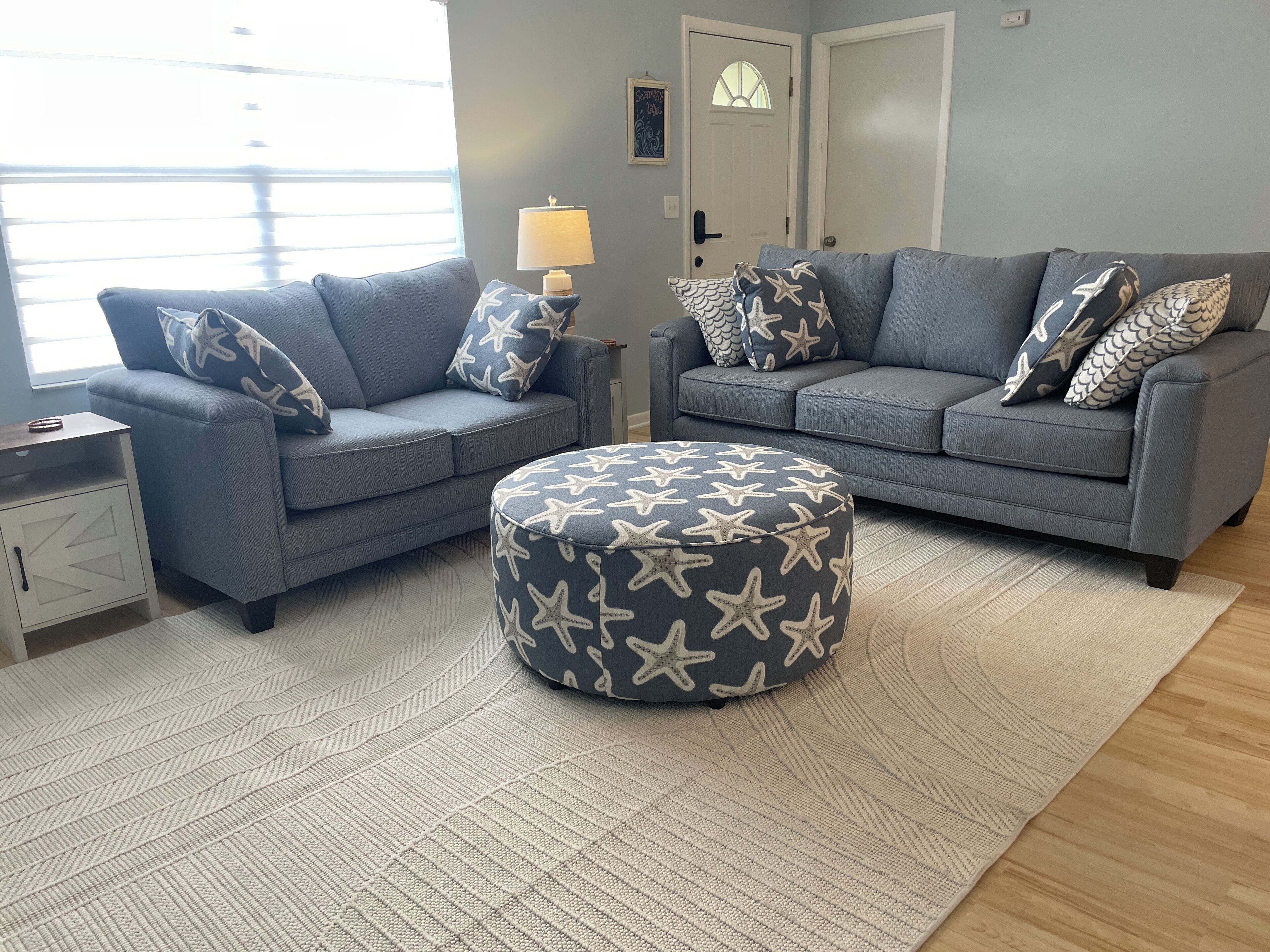 A living room with two grey sofas, star-patterned ottoman, and a lamp on a side table.