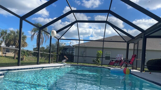 A clear swimming pool with a metal roof structure, surrounded by a grassy area and palm trees. - Private Heated Screened Pool,  10 min to Beach, Coastal, Comfy, 3Bd/2B, Quiet
 (Sebastian)