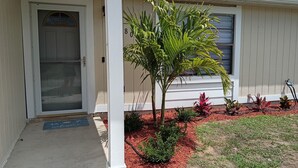 A house with a white exterior, a door with a glass panel, and a small tree in the front yard. - Private Heated Screened Pool,  10 min to Beach, Coastal, Comfy, 3Bd/2B, Quiet
 (Sebastian)