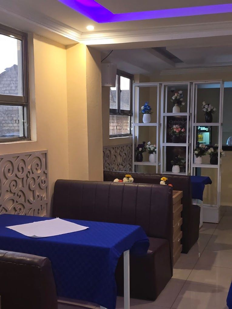 Interior de restaurante com área de cabines, uma mesa com toalha azul e uma estante decorativa com flores.