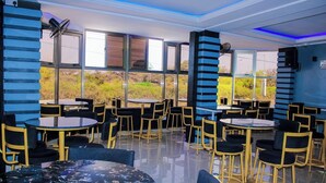 A modern indoor dining area with round tables and chairs, large windows, and a blue and black color scheme. - Desert Sky Hotel (Isiolo)