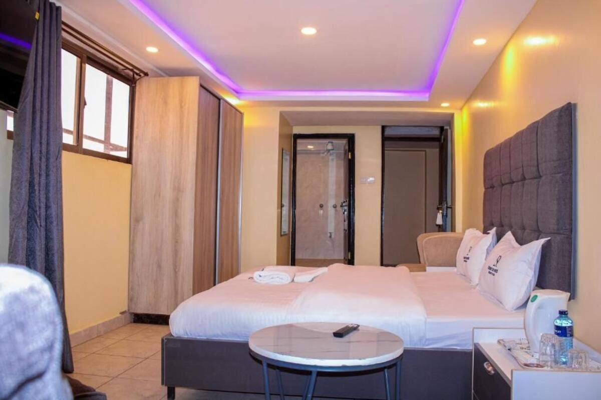 A hotel room with a large bed, a bedside table with a remote control, a small round table, and a bathroom door.