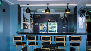A bar area with a counter, shelves of bottles, and a refrigerator. There are six chairs and a round table in front of the bar. - Desert Sky Hotel (Isiolo)