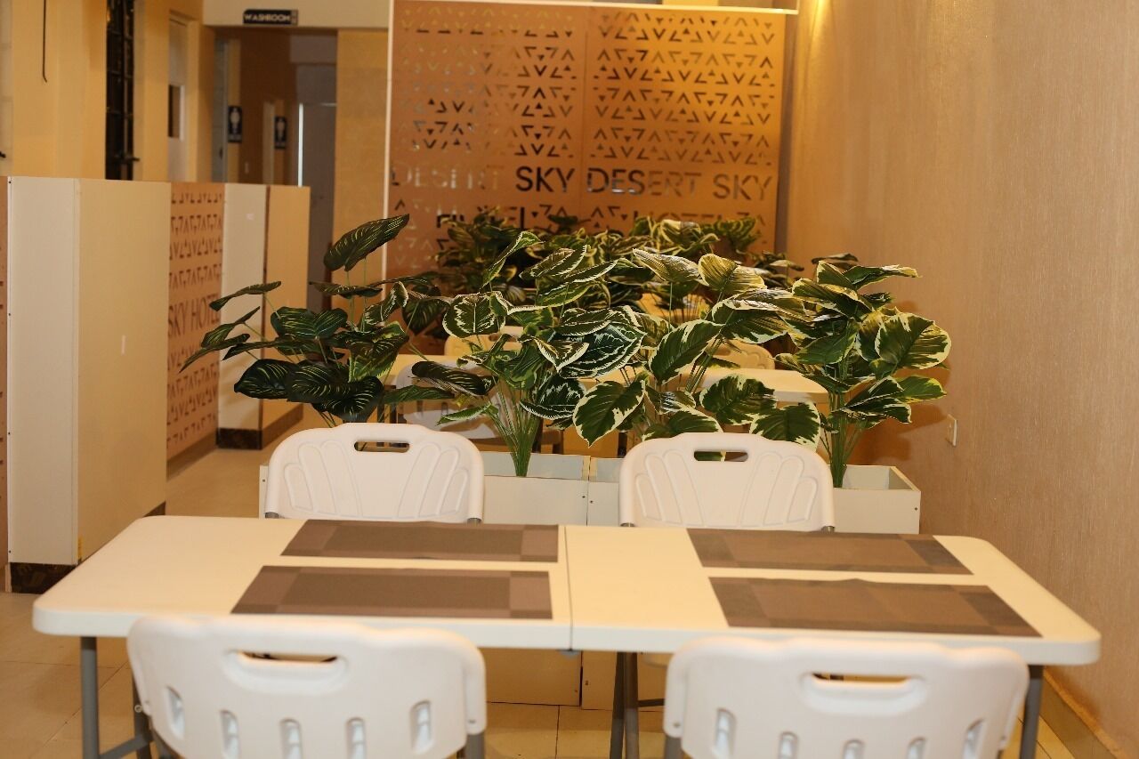 A room with a table and chairs, a large potted plant, and a wall with text.