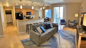 A modern kitchen with a central island, a grey sofa with patterned cushions, and a dining area with a table and chairs. - 1-Bedroom Condo in the Heart of the City (Salt Lake City)
