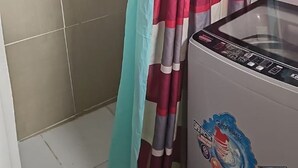 A bathroom with a shower curtain, a washing machine, and a tiled wall. - Charming 1-bedroom Loft apartment with AC in Herstelling Demerara. (Herstelling)