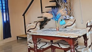 A dining area with a wooden table and chairs, a vase with dried plants, and a staircase in the background. - Charming 1-bedroom Loft apartment with AC in Herstelling Demerara. (Herstelling)